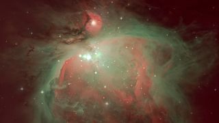 The swirling mass of interstellar dust and gas that forms the Orion Nebula is pictured glowing against the blackness of space. A collection of particularly bright stars are visible in the center of the nebula, surrounded by a radiation-sculpted cavity.