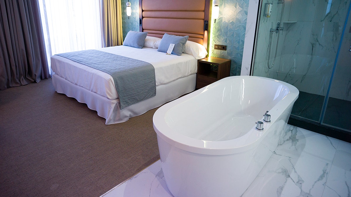 Hotel tub seen near bed in hotel room in Spain, with show in background