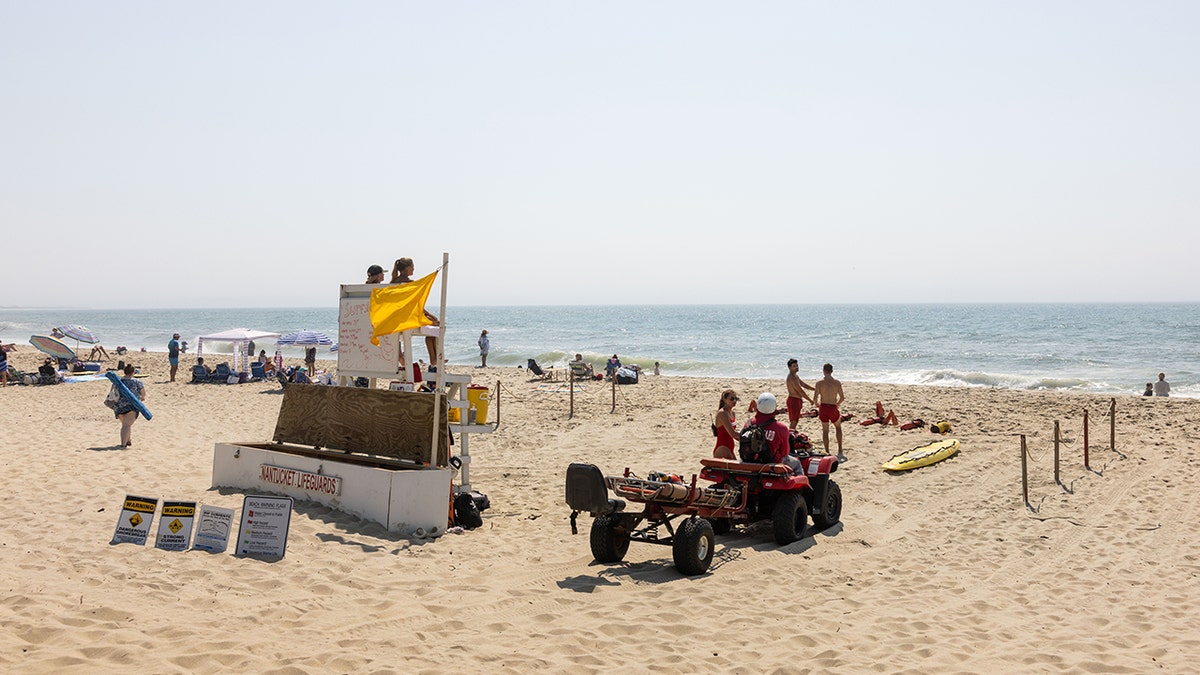 Lifeguard chair with yellow flag on a Nantucket beach with people sitting in beach chairs beside it