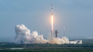 a white and black rocket lifts off from its launch pad, leaving a large white plume