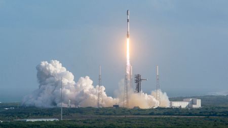 a white and black rocket lifts off from its launch pad, leaving a large white plume