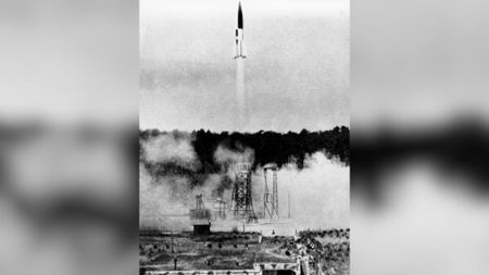 A black and white photo shows a small rocket launching from the ground